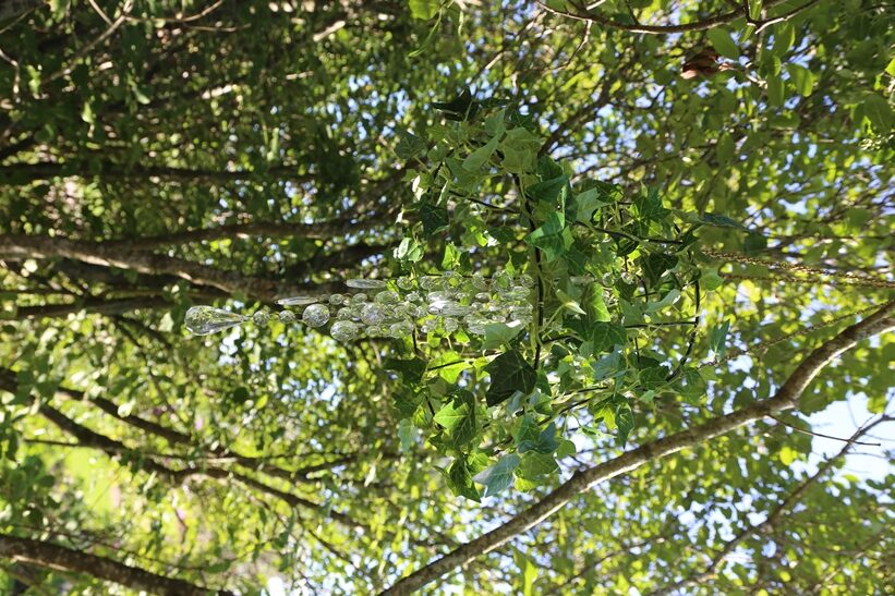 Salaisen puutarhan oksistosta roikkuu kristallilamppu.