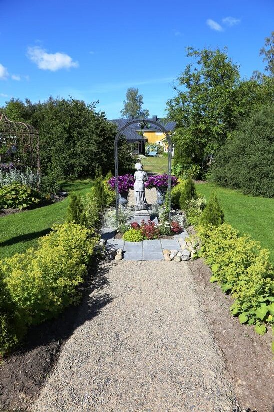 Korkeamäkien puutarhan pääväylä johtaa Lintukodosta Kaukametsään. Portti patsaineen ja istuksineen on rakennettu polulle. Polkua reunustavat jättipoimulehdet (Alchemilla mollis).