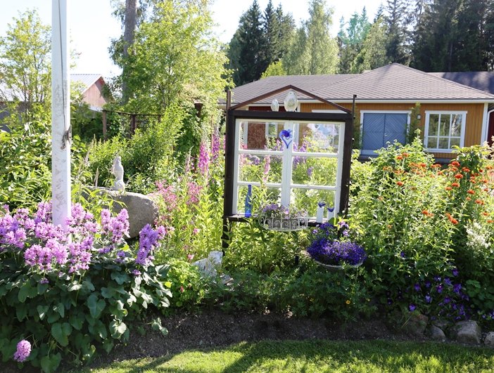 Ikkunan ympärillä olevassa ryhmässä kukkivat vasemmalla jalopähkämö (Stachys macrantha), ikkunan takana on sormustinkukkia (Digitalis purpurea) ja oikealla puolella palavaarakkautta (Lychnis chalcedonica) sekä valkokukkaisia akileijoja (Aquilegia-lajike).