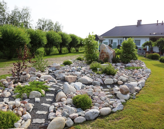 Luonnonkivien väliin on perustettu polkuja. Kivien väleissä kasvaa pieniä angervopensaita ja ryömiviä havuja, lähempänä taloa on korkeita lumipalloheisiä. Punalehtinen taimi on punakoivu.