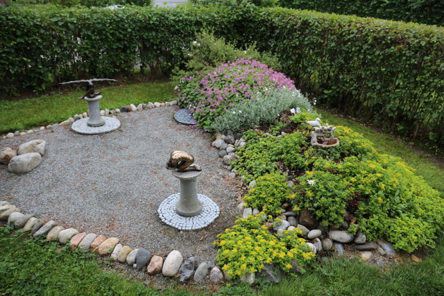 Matkoilta Airolat ostava patsaita ja muita koristeita. Pientä patsasaluetta rajaavaa kumparetta peittävät kulta- ja kaukasianmaksaruoho, hopeahärkki ja peittokurjenpolvi sekä valkokukkainen pensashanhikki ’Abbotswood’.